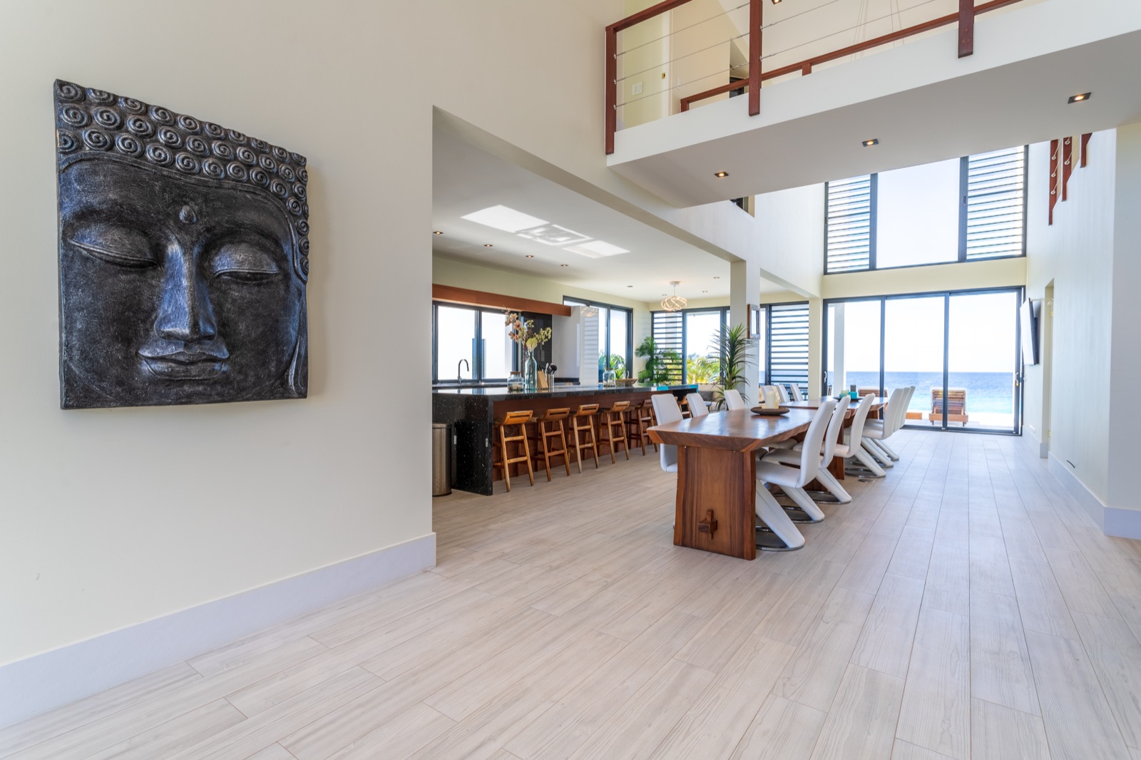 Luxury Bonaire villa with open-concept dining room and kitchen, featuring a natural wood table, double-height ceilings, and floor-to-ceiling glass doors with a panoramic ocean view.